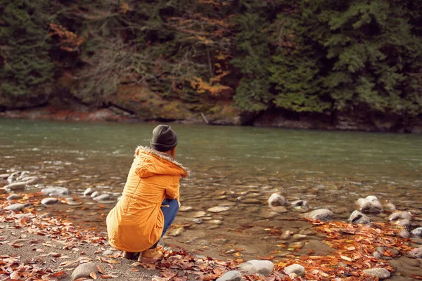 Vrouw in een gele jas in de buurt van de rivier bewondert de natuur Herfst bos — Stockfoto