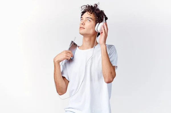 Homem com cabelo encaracolado em t-shirt branca ouvindo música com tecnologia de fone de ouvido — Fotografia de Stock