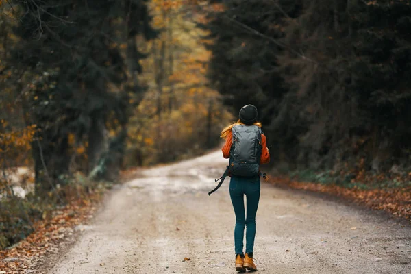 Felice escursionista donna con zaino passeggiate sulla strada nella foresta autunnale — Foto Stock