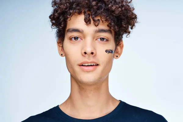 Curly-haired guy in a black t-shirt cosmetics on the face clean skin — Stock Photo, Image