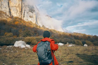 Sonbaharda sırt çantalı gezgin dağlarda mavi gökyüzü yüksek kayalıkları bulutlandırır.