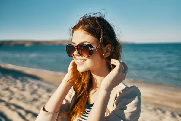 Viajero en una chaqueta beige y gafas de sol en la arena cerca del mar en la playa —  Fotos de Stock