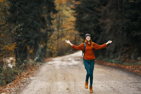Felice escursionista donna con zaino passeggiate sulla strada nella foresta autunnale — Foto Stock