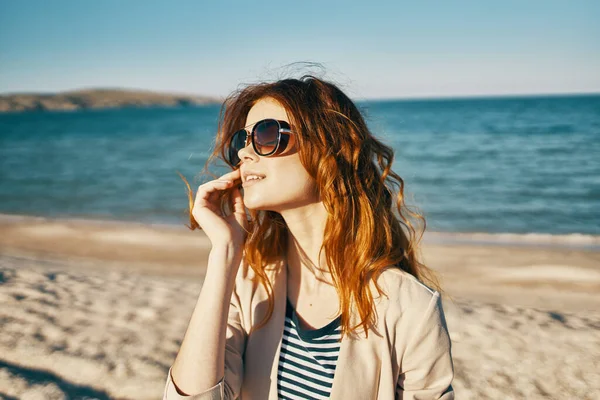 Kobieta w czerwonych włosach i okularach słonecznych śmieje się w przyrodzie na plaży w pobliżu morza — Zdjęcie stockowe