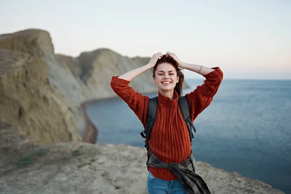 Eine Reisende im Pullover mit Rucksack gestikuliert mit ihren Händen in der Nähe des Meeres in der Natur — Stockfoto