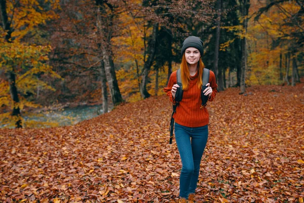 Podróżnik z plecakiem w jesiennym lesie i kapeluszem dżinsy sweter spadł liście drzewa jeziora — Zdjęcie stockowe
