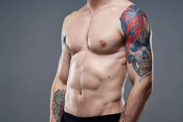 Sporty man with pumped up abs tattoos on his arms gray background muscles — Stock Photo, Image