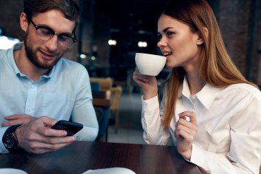 Masada kahve içen bir kadın, iş arkadaşı teknolojisinin yanında çalışıyor.