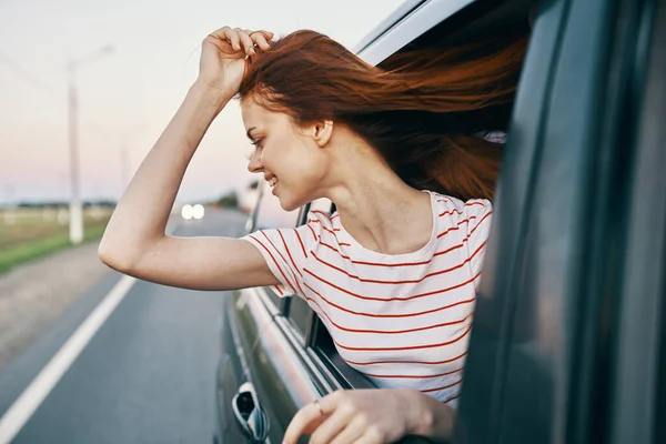 Enérgico vermelho-haired t-shirt mulher espreitando para fora da janela do carro aberto na estrada trilha viagem — Fotografia de Stock