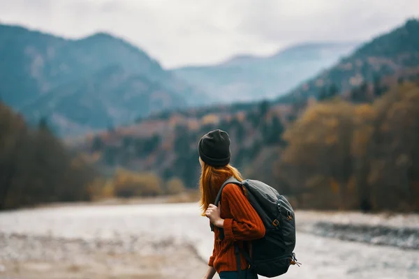 Donna in un cappello con uno zaino stanno riposando in montagna nella natura vicino al fiume — Foto Stock