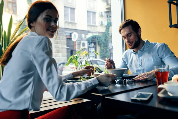 En kvinna i en lätt skjorta och en affärsman äter lunch vid ett bord i ett café läckra mat drycker anställda — Stockfoto