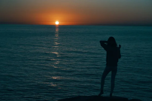 Femme dans les montagnes au coucher du soleil près de la mer leva les mains vers le haut — Photo