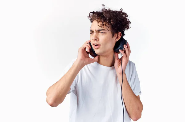 Emotionele man met krullend haar in hoofdtelefoon luistert naar muziek op een lichte achtergrond — Stockfoto