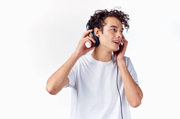 Chico emocional con el pelo rizado en los auriculares escucha música sobre un fondo claro — Foto de Stock