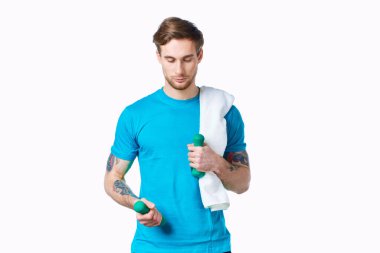 Elinde dambıllar, omuzlarında havluyla egzersiz yapan sportif bir adam.