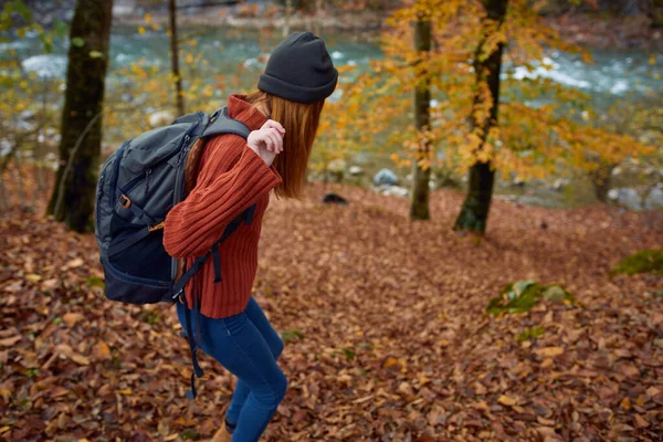 山の中の川の近くにリュックを背負ったセーターの女性公園の木々秋の風景 — ストック写真