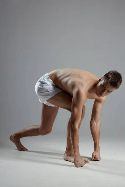 Homem fazendo esportes dentro de casa em shorts brancos inclinando-se para a frente vista lateral — Fotografia de Stock