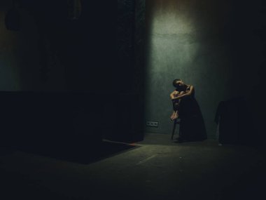 Bir kadın elleriyle bacaklarına sarılır ve karanlık bir odada oturur. Yalnızlık depresyonu.