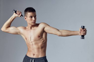 Elinde dambıllar olan atletik yapılı bir adam.