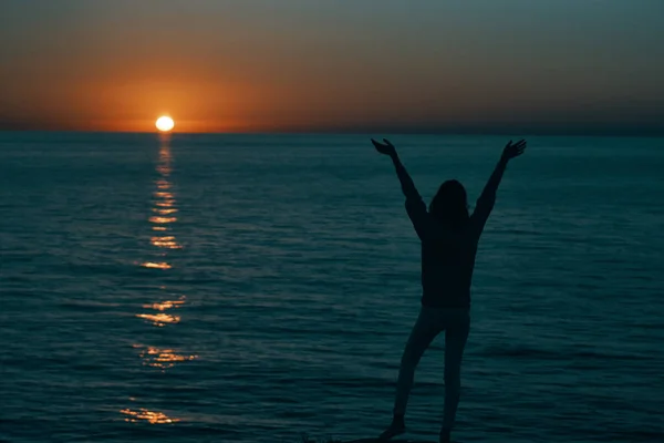 Femme dans les montagnes au coucher du soleil près de la mer leva les mains vers le haut — Photo