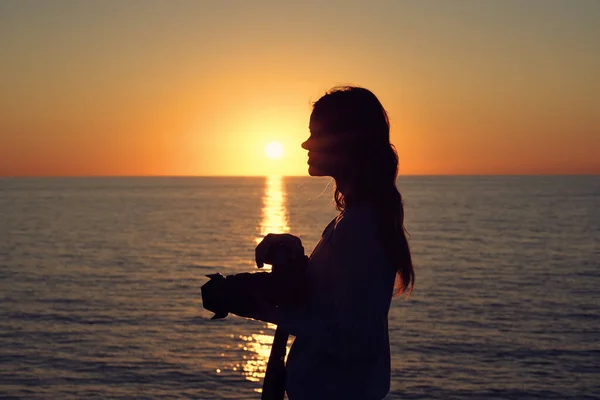 Silhouette of a woman with a camera at sunset near the sea side view — Stock Photo, Image