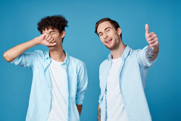 같은 셔츠와 티셔츠를 입은 젊은 남자들이 파란 배경 친구들에게 손을 흔들고 있습니다. — 스톡 사진