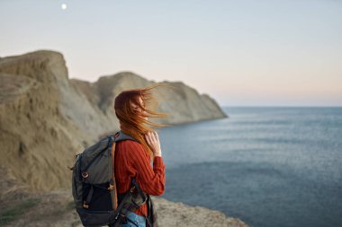 Sırtında bir sırt çantası olan kızıl saçlı gezgin, uzaktaki dağlara ve denize bakıyor.