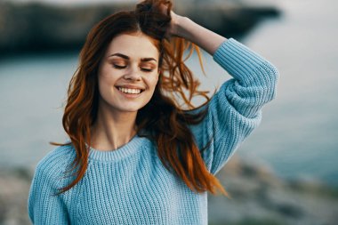 Elinde saç tutan gülümseyen kadın doğa turizmi sallıyor.