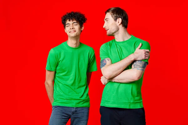 Amici gioiosi in t-shirt verdi sono in piedi accanto allo sfondo rosso — Foto Stock