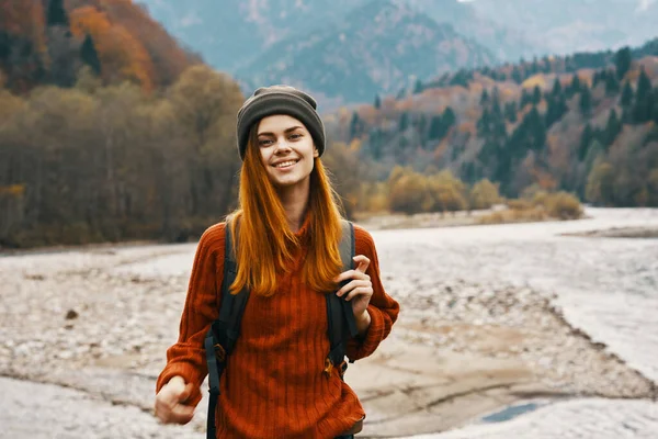 Kobieta w swetrze kapelusz z plecakiem spoczywa w pobliżu rzeki w górach na krajobraz przyrody — Zdjęcie stockowe