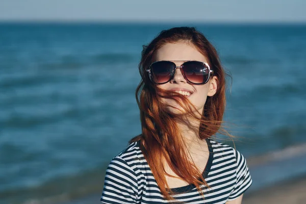 Vacker kvinna i solglasögon vid havet i bergen rött hår randig t-shirt — Stockfoto