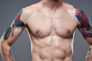 Kollarında şişirilmiş karın kasları olan sportif bir adam. Gri arka plan kasları.