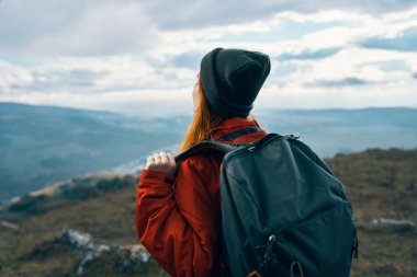 Sırt çantalı, turistik dağ manzaralı, sıcak elbiseli enerjik bir kadın.