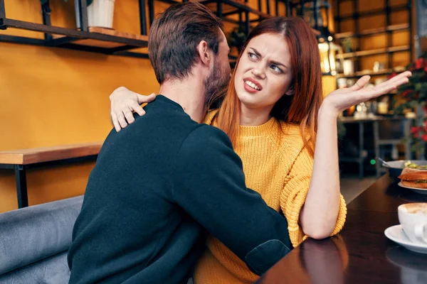 Una mujer con asco abraza a un hombre en un suéter en una mesa en un café — Foto de Stock