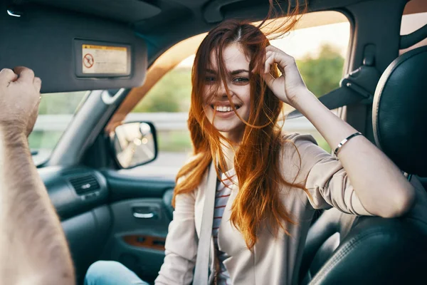 Ευτυχισμένη κοκκινομάλλα γυναίκα σε ένα μπεζ παλτό στο μπροστινό κάθισμα του αυτοκινήτου χαμόγελο μοντέλο gesturing με τα χέρια του συντρόφου ταξιδιώτη — Φωτογραφία Αρχείου
