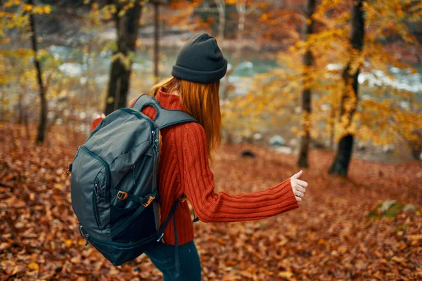 Wanderin mit Rucksack im Herbstwald nahe Gebirgsfluss und umgestürztem Laub — Stockfoto