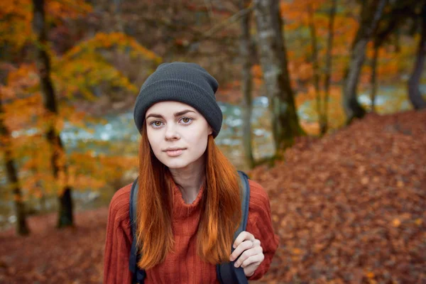 Die energische Touristin mit Rucksack, rotem Pullover und Mütze ruht im herbstlichen Wald im Park. — Stockfoto