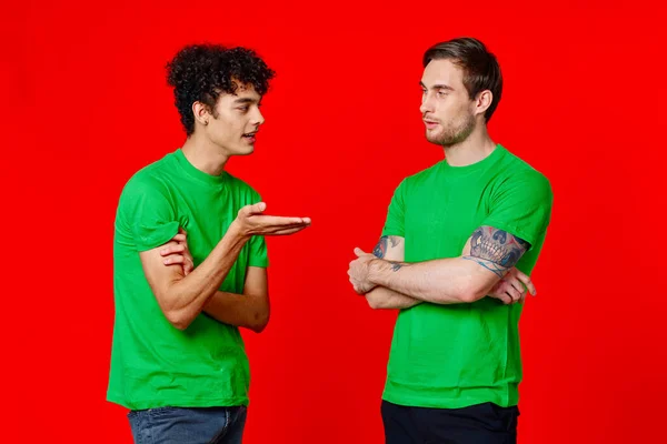 녹색 티셔츠를 입은 두 친구가 긍정적 인 빨간 배경의 긍정적 인 대화를 하고 있습니다. — 스톡 사진