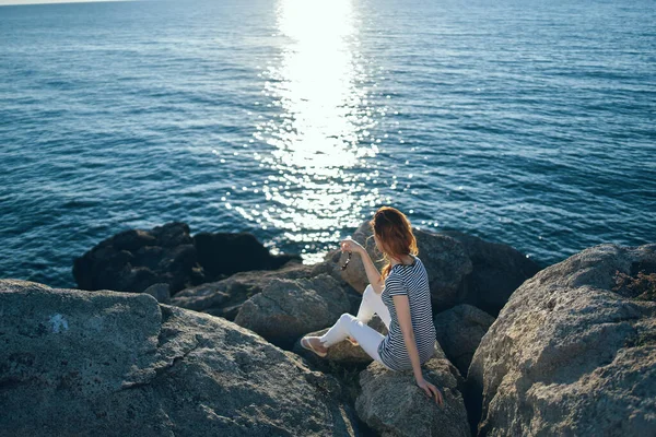 Mujer viajero sentado en piedras cerca del mar paisaje playa puesta del sol agua clara —  Fotos de Stock
