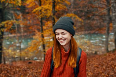 Sırtında sırt çantası olan şapkalı ve süveterli bir kadın. Eğlenceli sonbahar manzarası nehri.