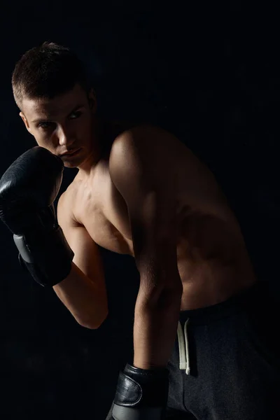 Boxeador en guantes negros doblado sobre un gimnasio culturista de fondo oscuro —  Fotos de Stock