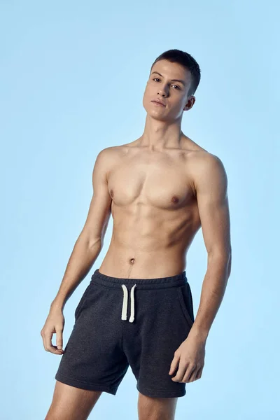 Athletic man with naked torso in black shorts bodybuilder posing blue background — Stock fotografie