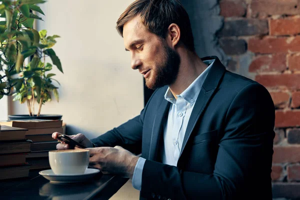 Homem de negócios em um terno sentado a uma mesa com uma xícara de café em um descanso de café — Fotografia de Stock
