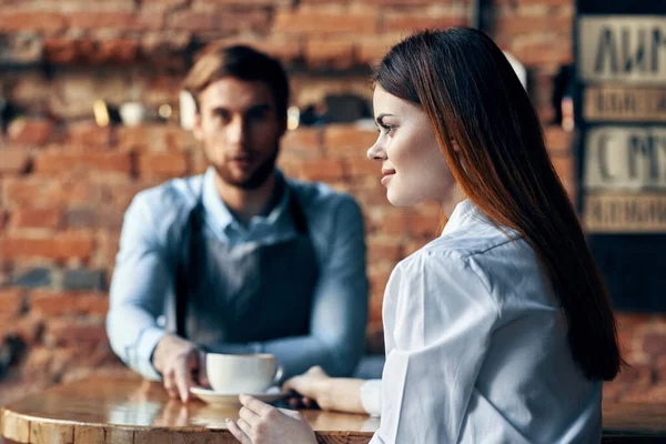 Bir fincan kahveyle mutlu bir kadın ve masadaki önlüklü bir erkek barmen. — Stok fotoğraf