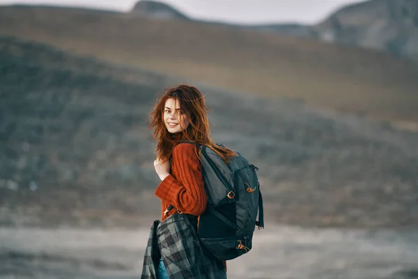 Kobieta w czerwonym swetrze z plecakiem spogląda wstecz na przyrodę w górach — Zdjęcie stockowe
