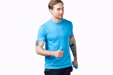 Bir adam elinde dambıllarla spor salonuna gider. Hafif bir arka plan ve dövme modeli.