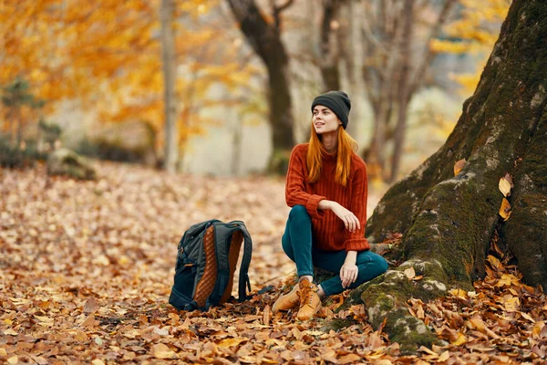 Mulher perto de árvore e mochila para viajar folhas caídas floresta de outono — Fotografia de Stock