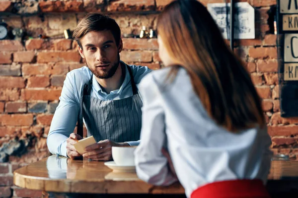 Kafe masasında bir fincan kahve ve önlüklü bir adam ve kırmızı etekli bir kadın. — Stok fotoğraf