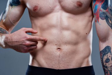 Karnında küpleri olan sporcu vücut kaslarını şişirmiş dövmeler çıplak gözle görünür.