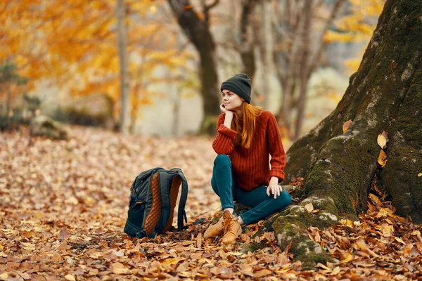 Kobieta w pobliżu drzewa i plecak dla podróżujących upadłych liści jesienny las — Zdjęcie stockowe